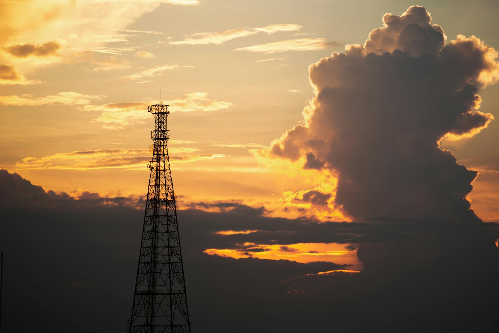 A transmission tower silhouetted against a vibrant Indian sunset with dramatic clouds.